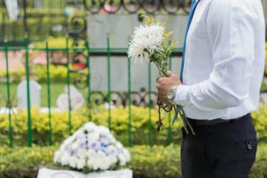 Foto, Mann steht am Grab mit Blumen